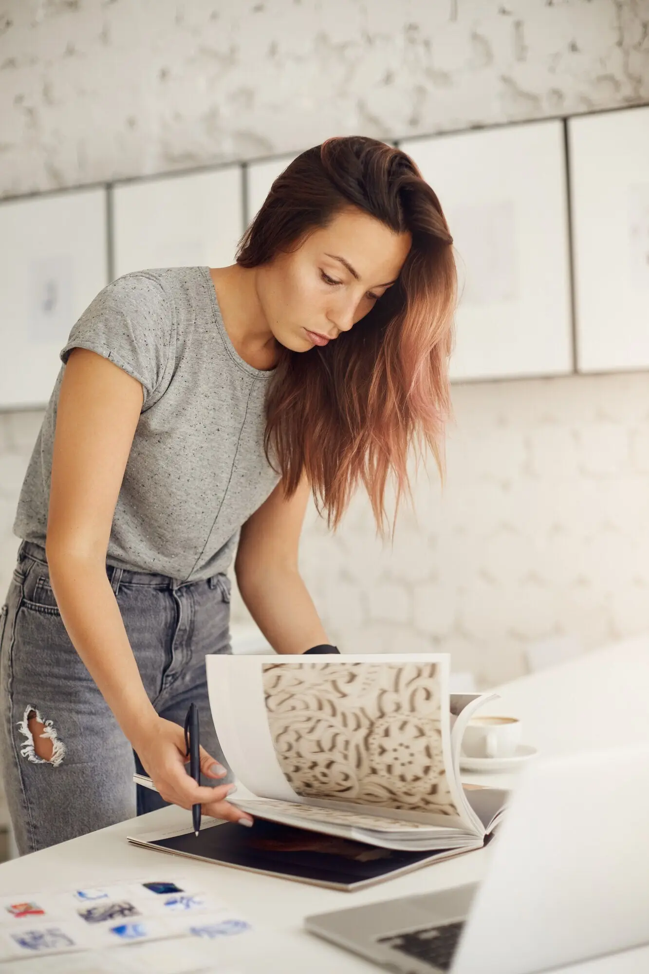 Junger Grafikdesigner blättert in einer Zeitschrift auf der Suche nach Inspiration für einen Kunden und nutzt dabei einen Laptop.